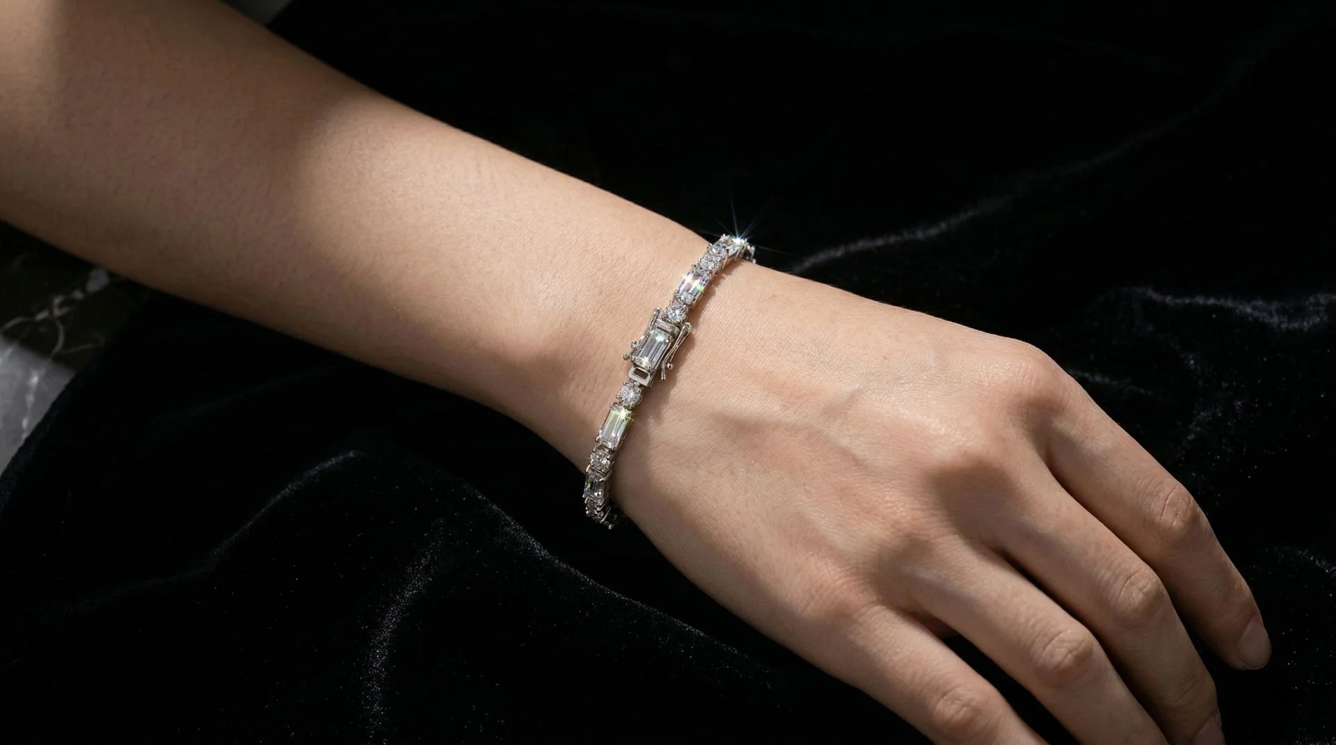 Close-up of a woman's wrist wearing a luxury silver crystal tennis bracelet with sparkling baguette stones against a dark background.